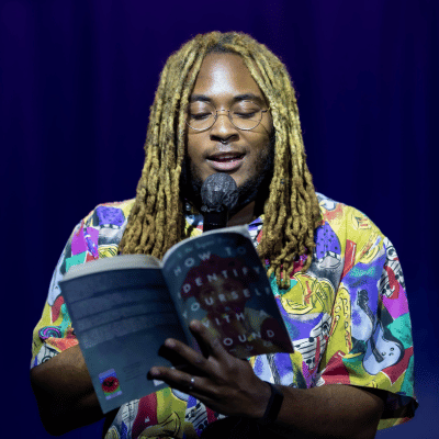 KB Brookins holds a mic while reading from their book How to Identify Yourself with a Wound